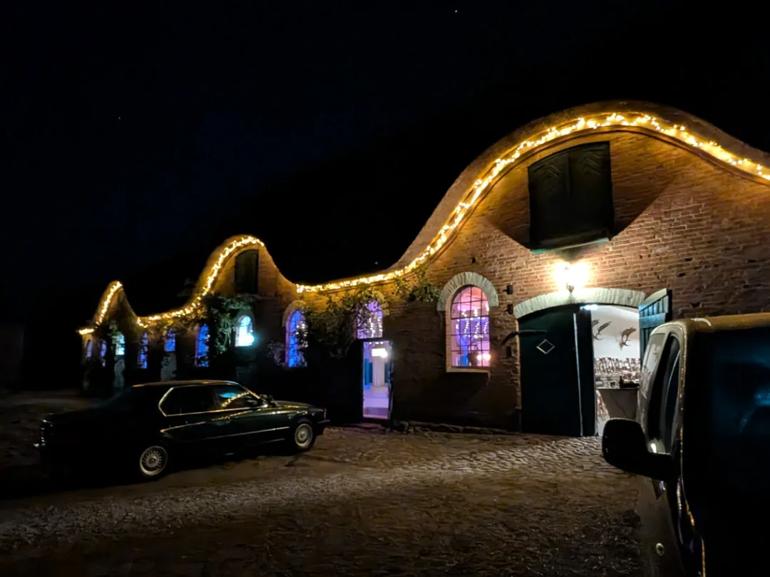 Festscheune von Gut Helmstorf bei Nacht, Lichterketten auf dem geschwungenen Giebel und bunt beleuchtete Rundbogenfenster während einer Hochzeitsfeier